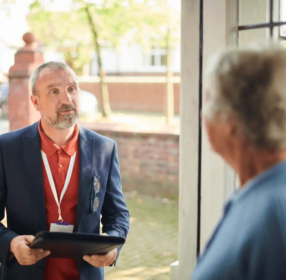 Man with a clipboard and lanyard speaks to a resident at their front door