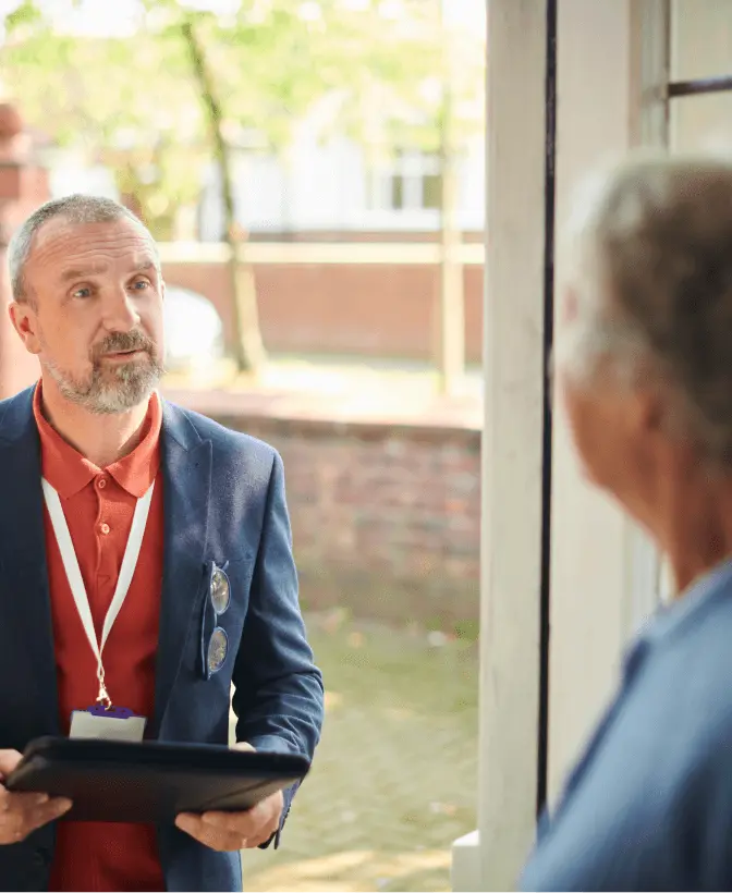 Man with a clipboard and lanyard speaks to a resident at their front door